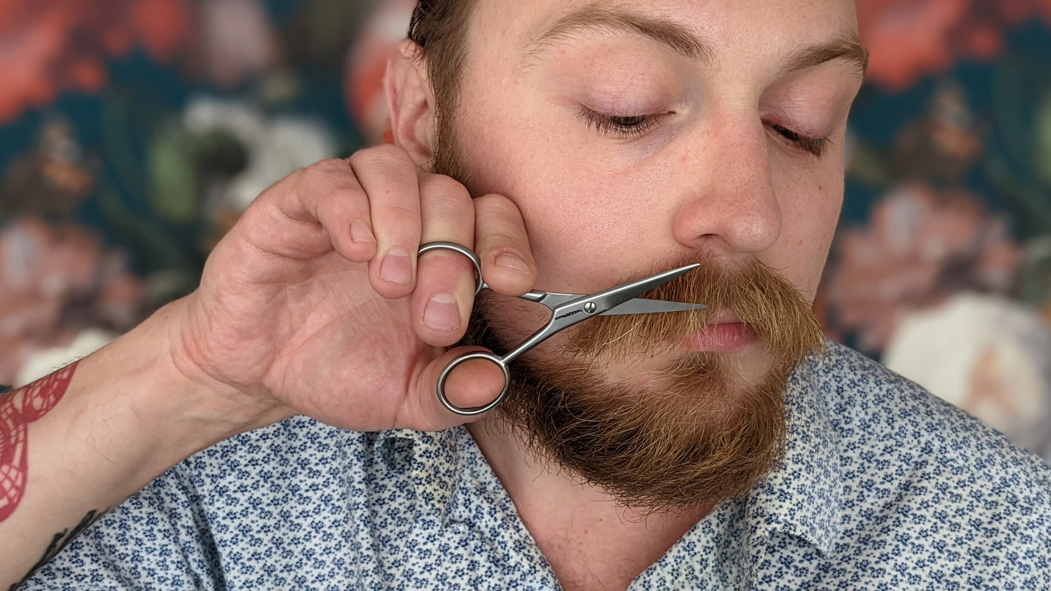 A person carefully trimming their mustache with small scissors while combing the hairs downward in a well-lit bathroom